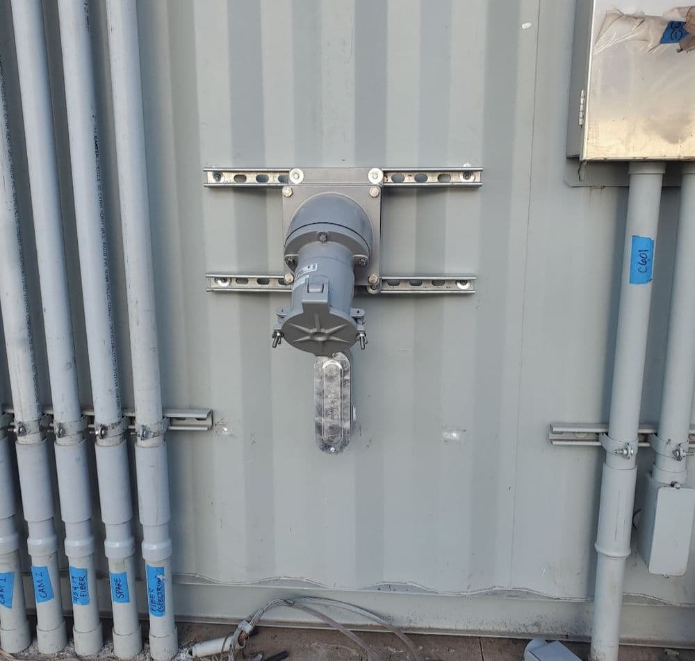 Electrical conduit with a mounted gray motor and transparent cover on a gray wall.
