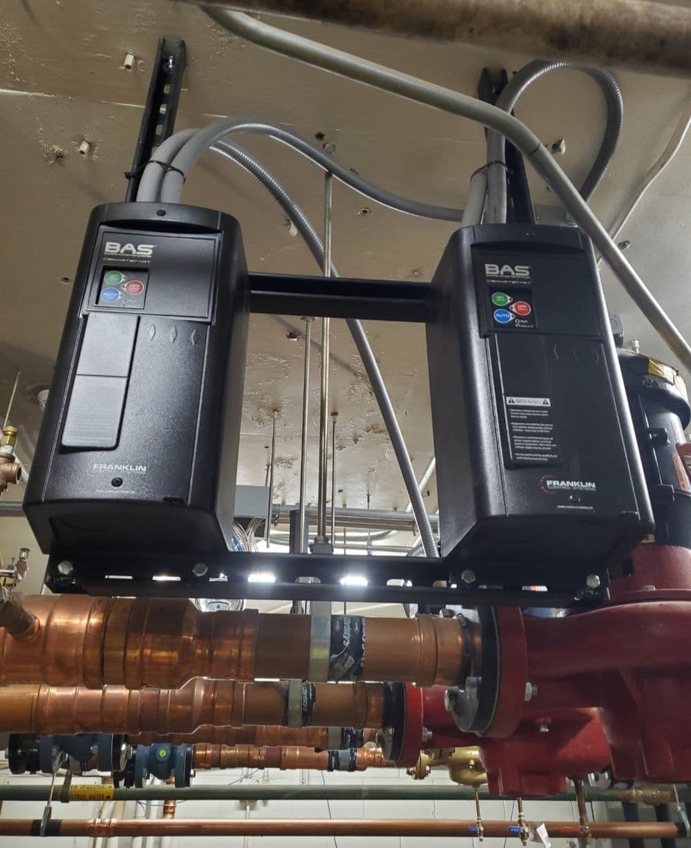 Two BAS control units mounted above copper piping in a mechanical room setting.