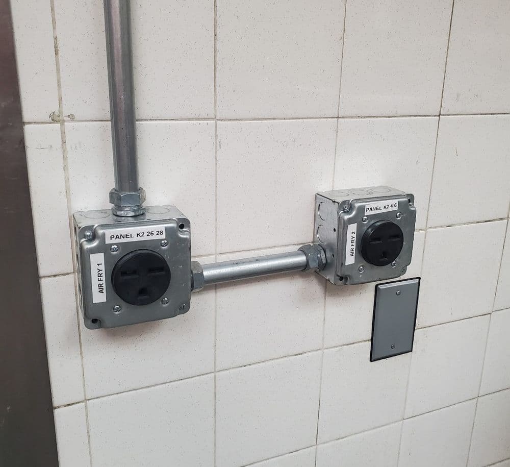 Electrical outlets mounted on a wall with labeled panel connections in a commercial setting.