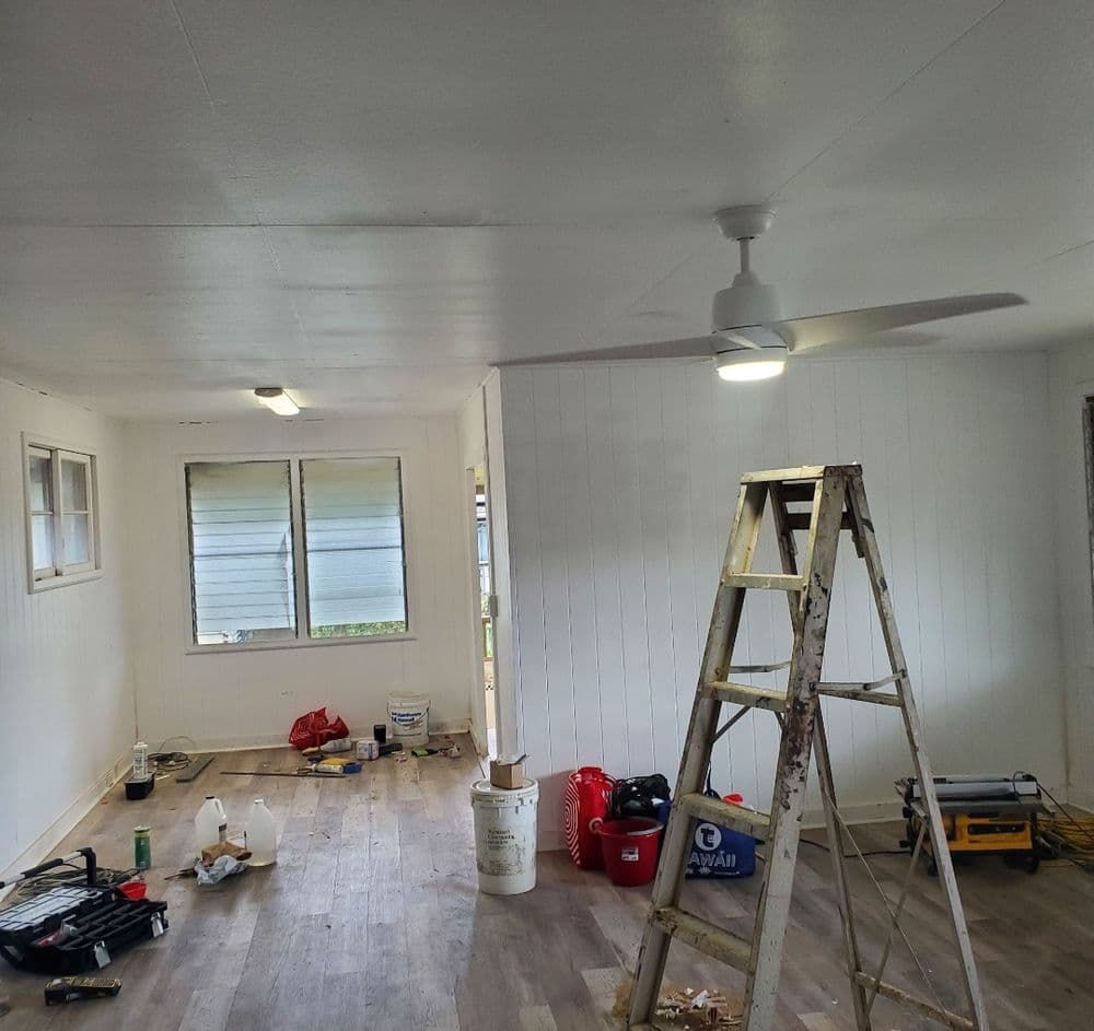 Renovated room with a ladder, ceiling fan, tools, and unfinished wall treatment.
