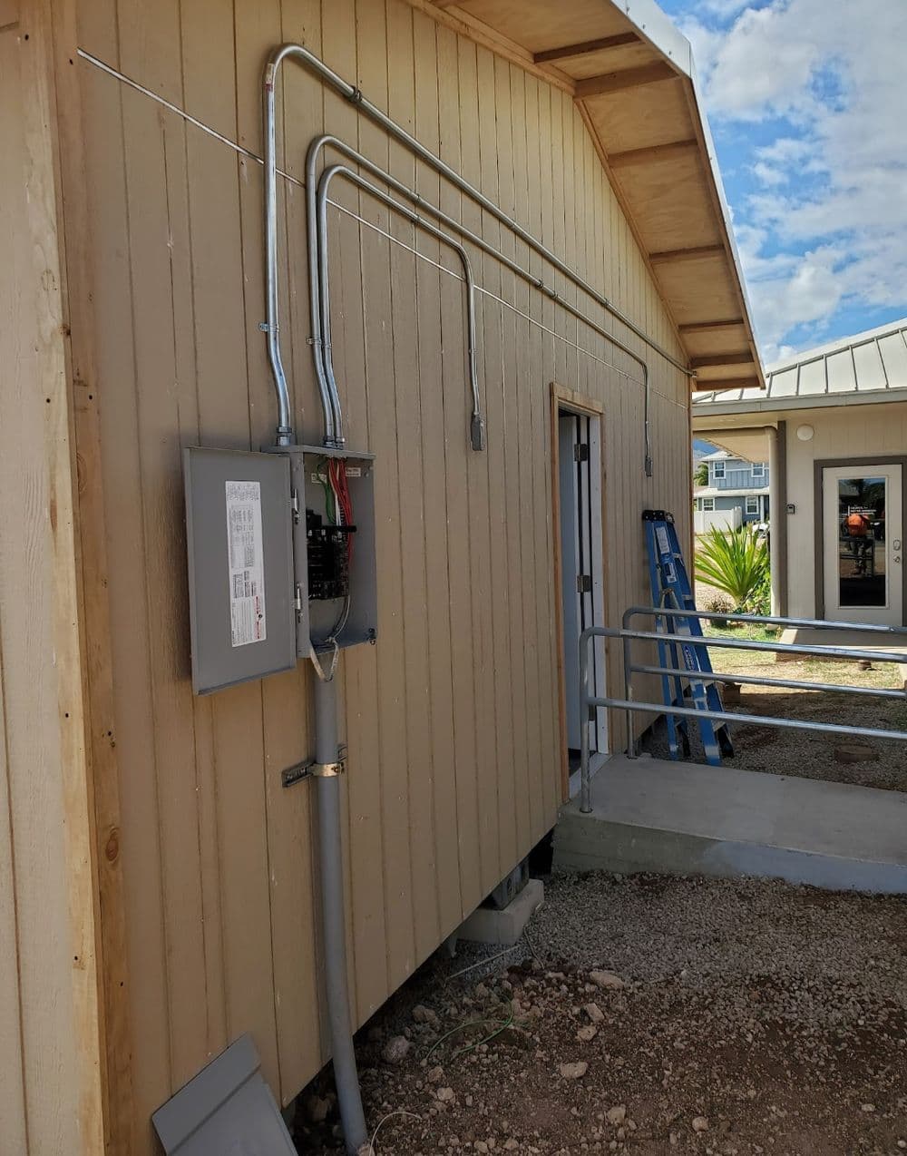 Electrical panel installation on a wooden building exterior with conduit and ladder nearby.
