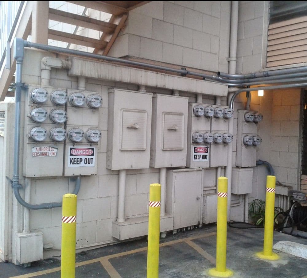 Utility meters on a building wall with warning signs and yellow safety posts.