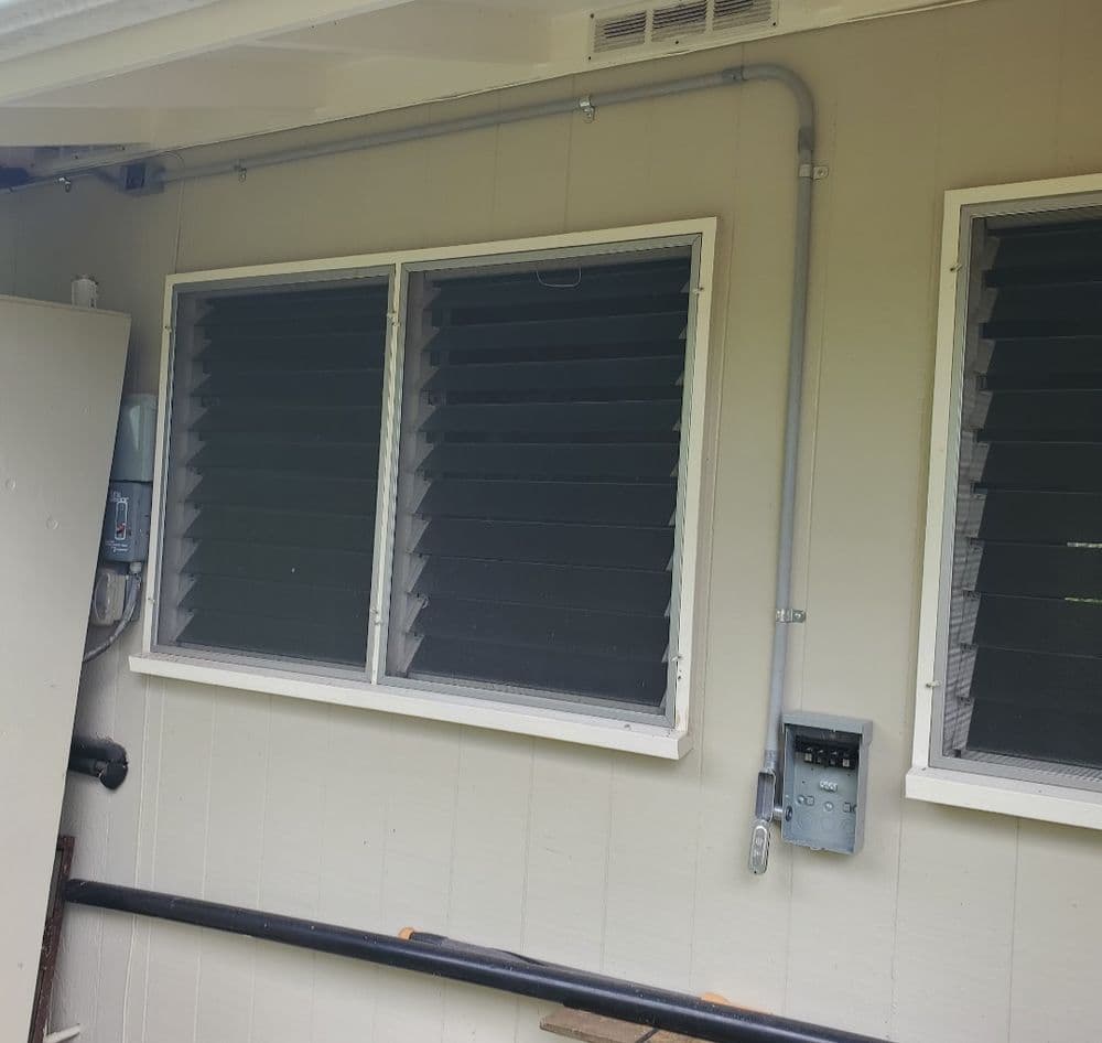 Exterior view of a house showing closed windows, electrical meter, and wall-mounted pipes.