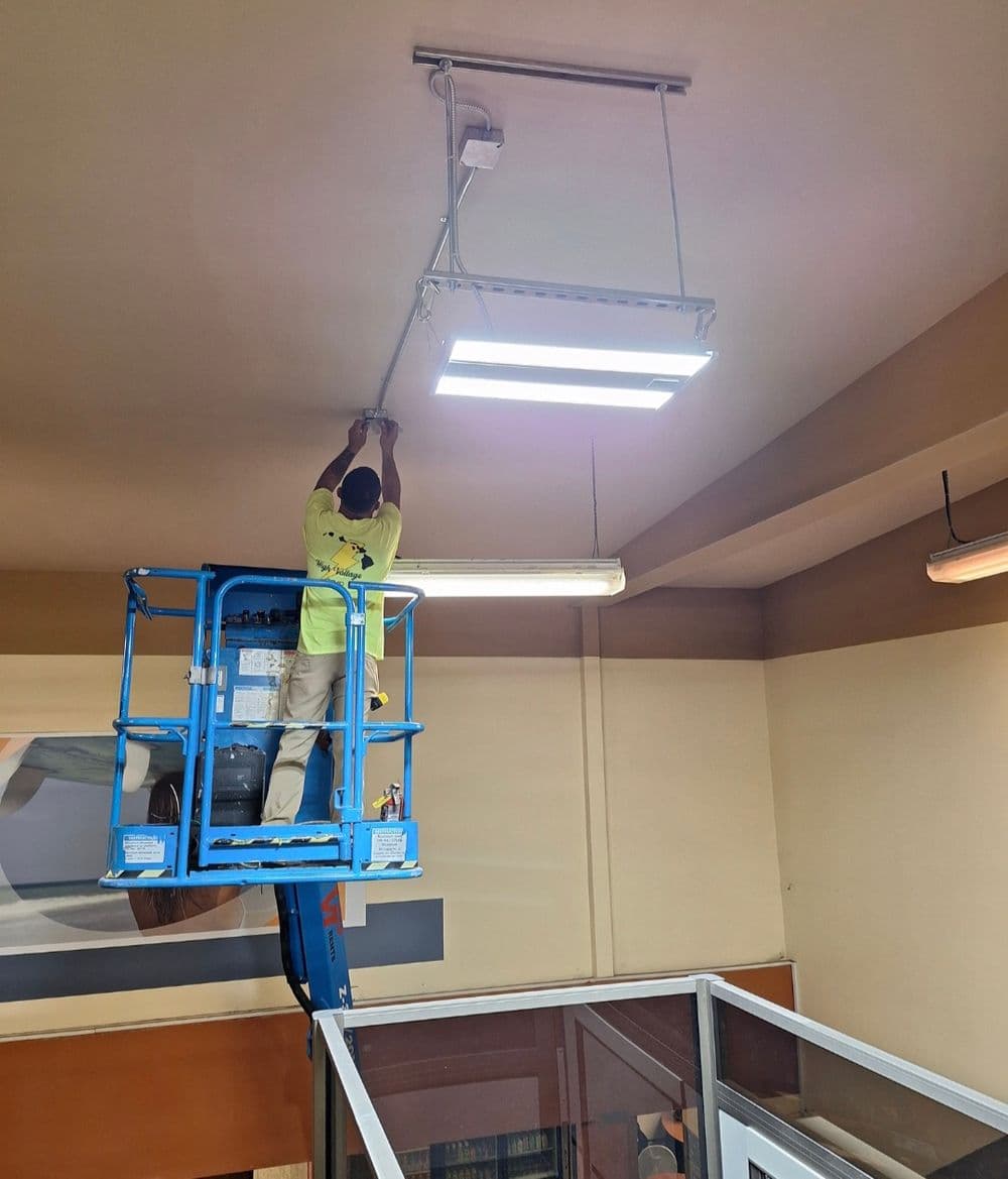 Worker using a lift to install ceiling lights in an office space.