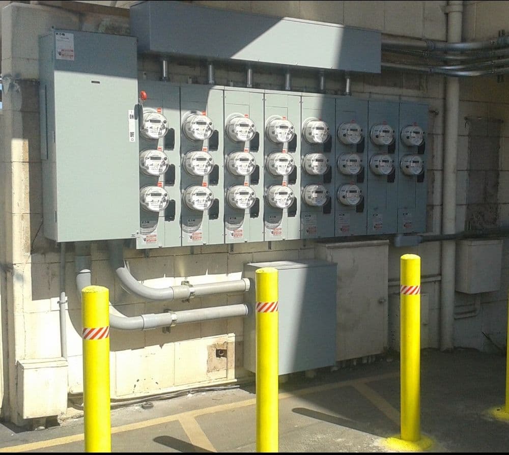 Row of electrical meters mounted on a wall, yellow poles providing safety barriers.