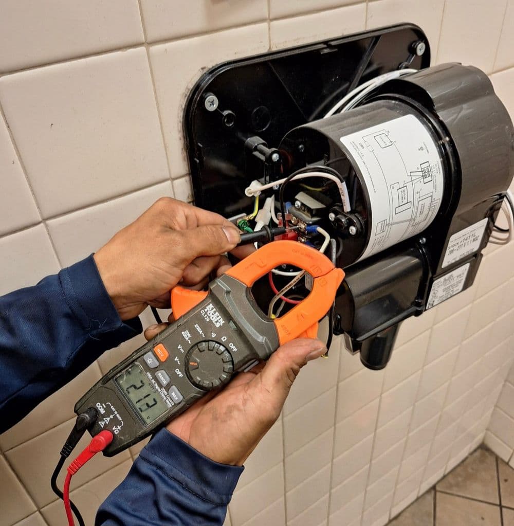 Electrician using a multimeter on a motor circuit mounted on a wall.