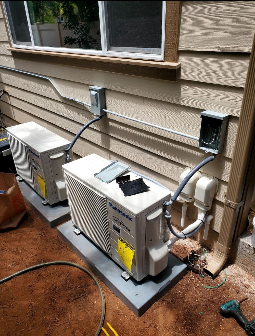 Two Panasonic air conditioning units installed outside a home, connected with electrical wiring.
