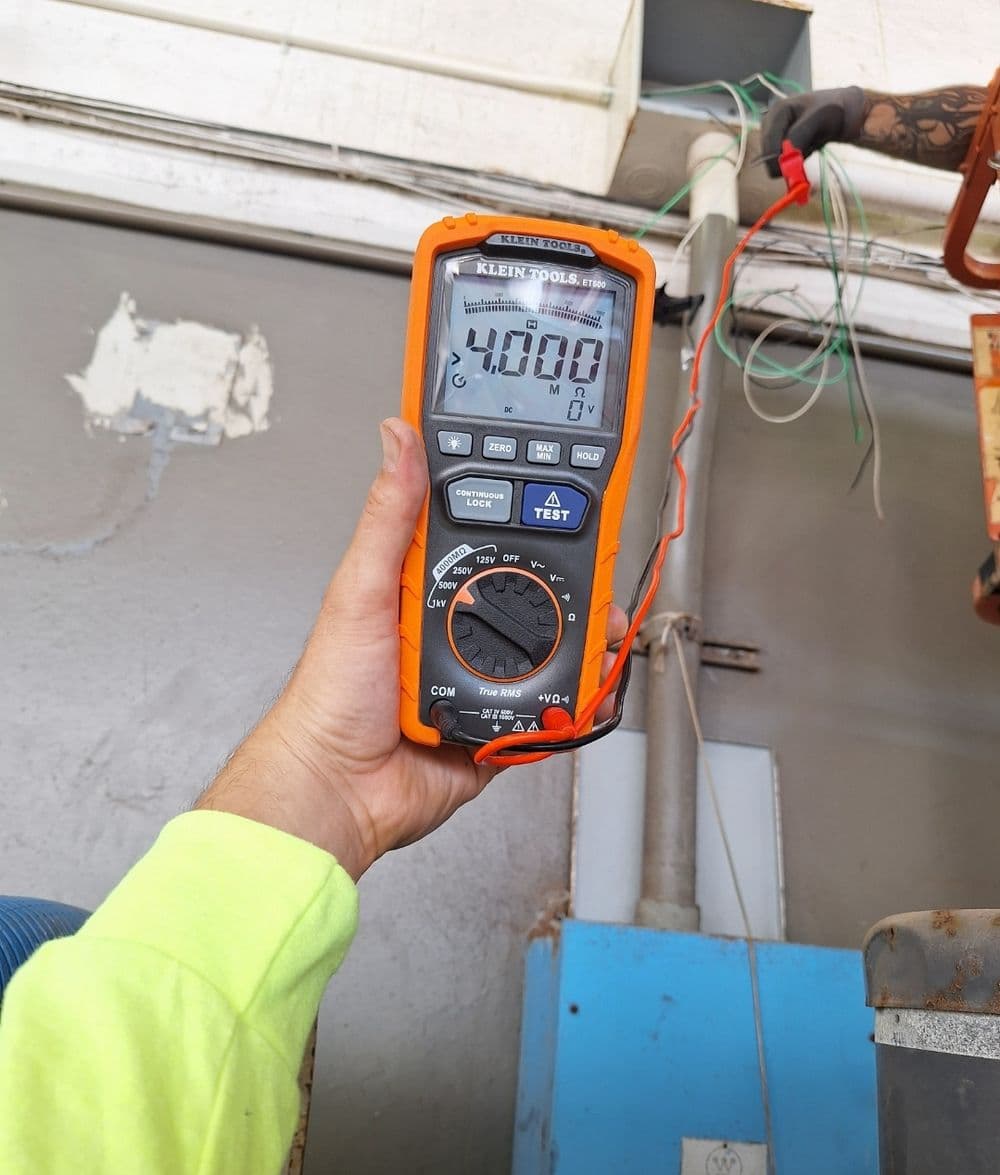 Person holding a Klein Tools multimeter reading 400.0 with electrical wires in background.