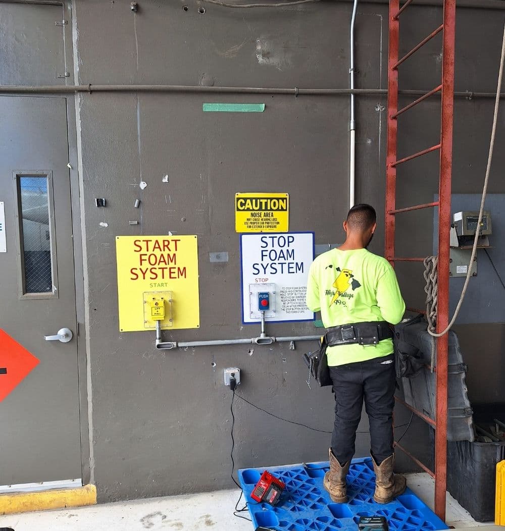 Worker monitoring fire foam system controls on a building wall with safety signs.