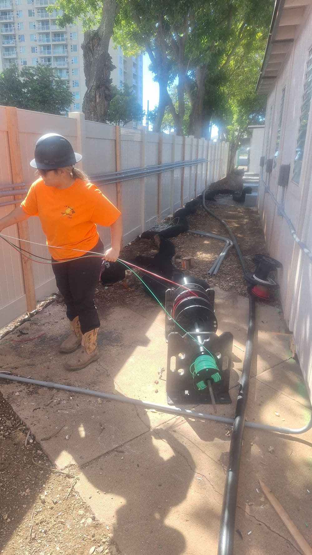 Worker in an orange shirt using equipment to install cables outside a building.