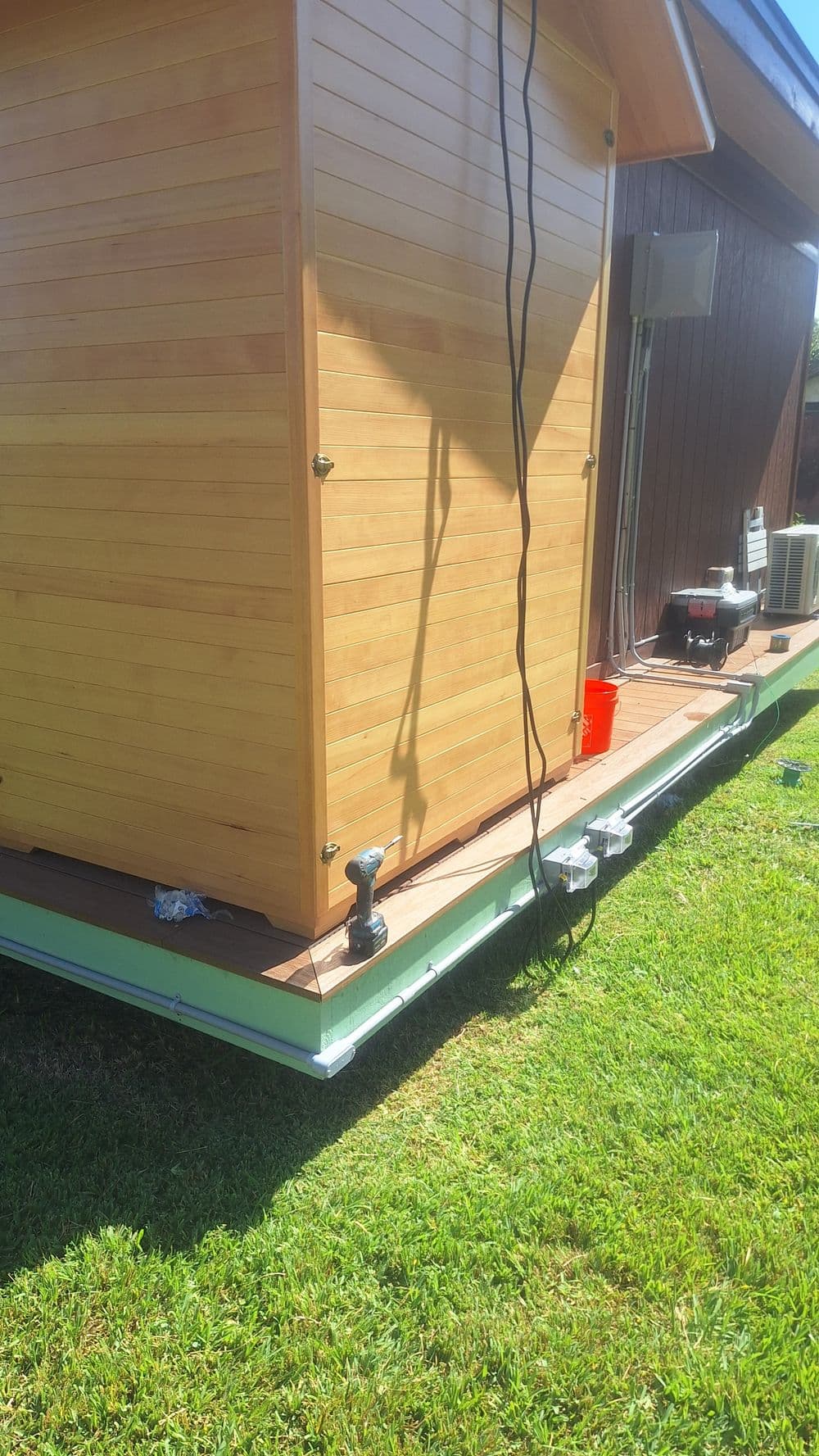 Side view of a wooden shed on a grass lawn, showcasing exterior details and equipment.
