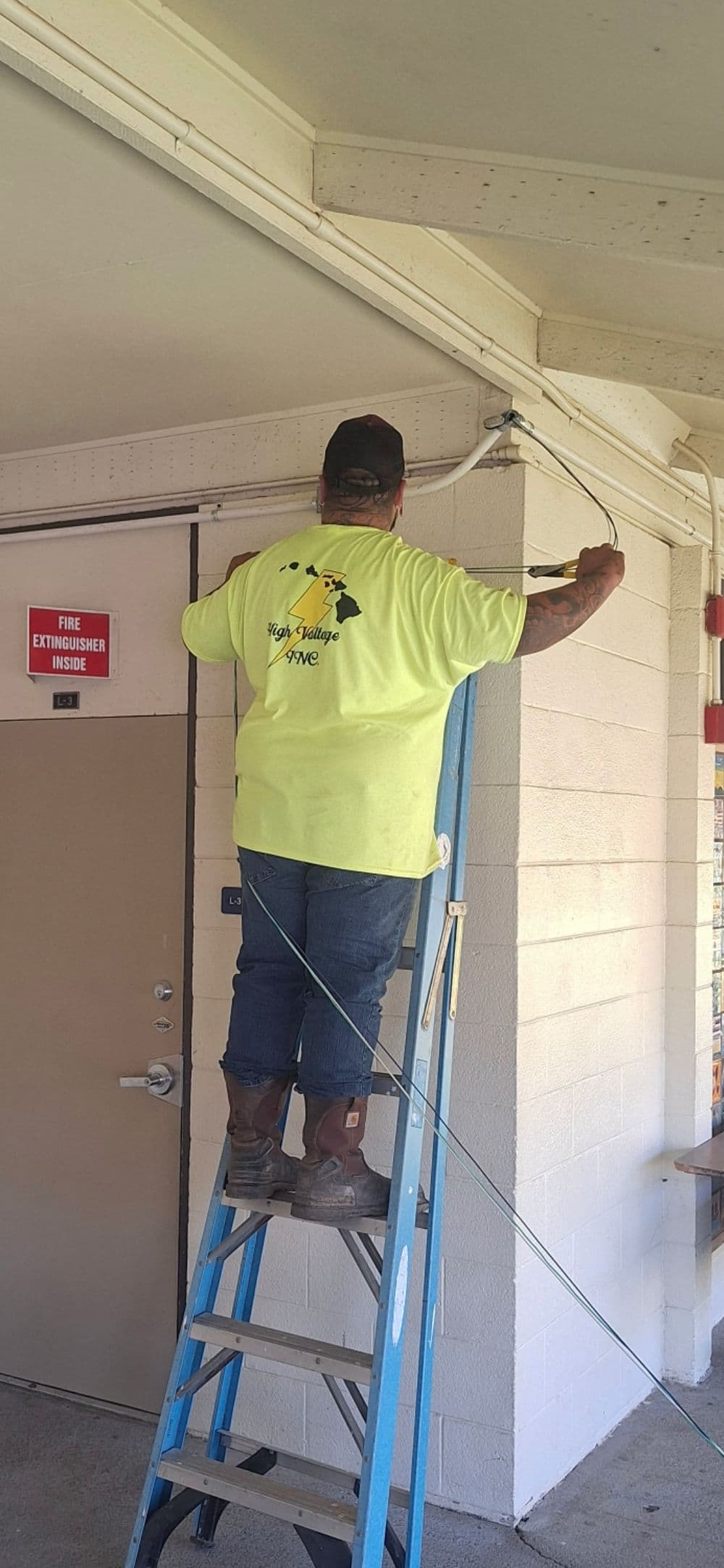 Worker in a neon yellow shirt installing equipment on a building, using a ladder.