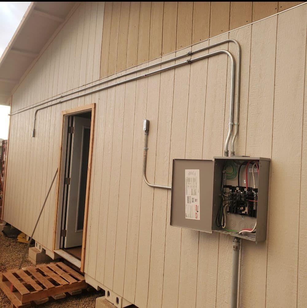 Electrical installation on exterior wall of a building with a service panel and conduit.