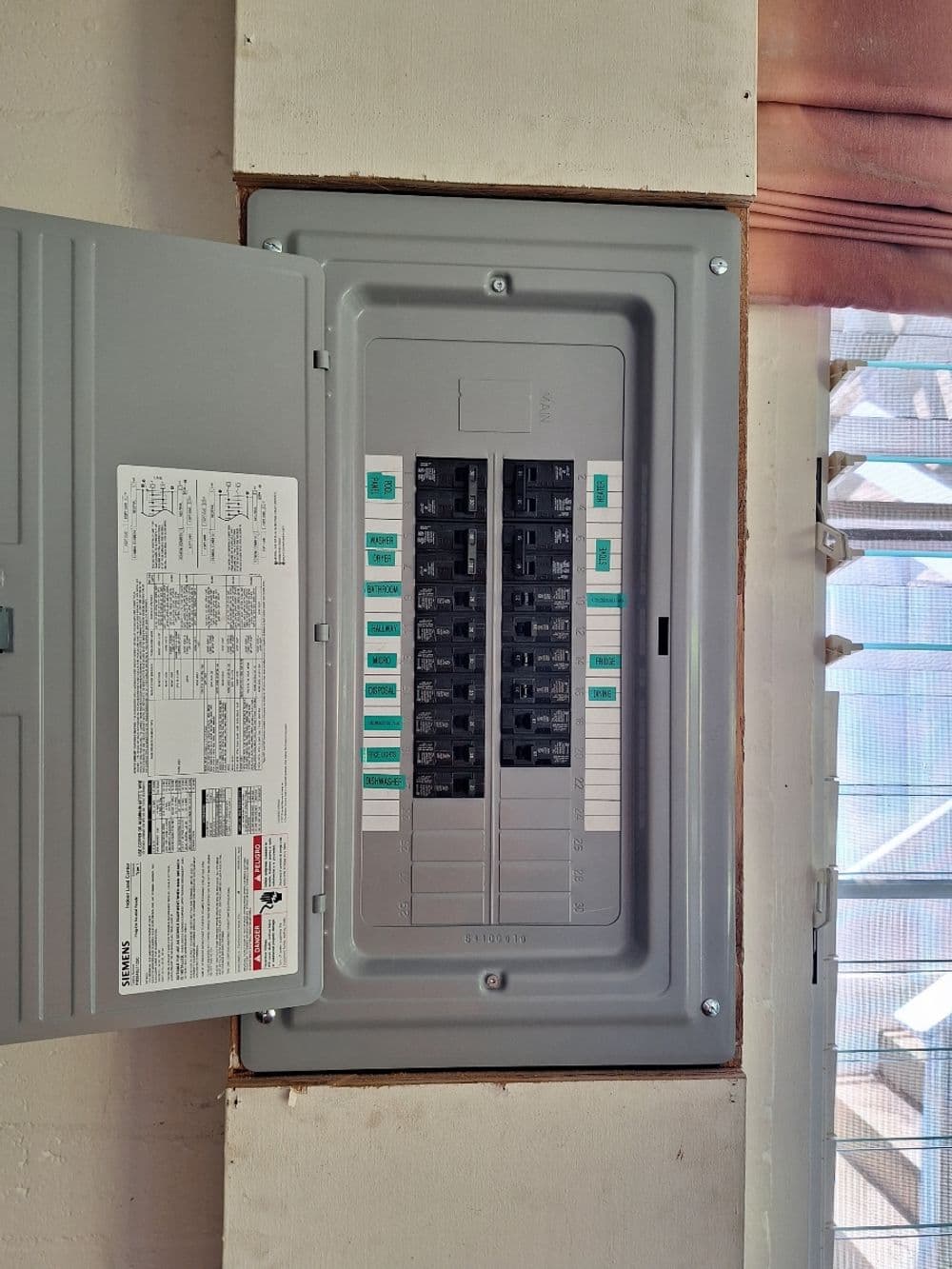 Electrical panel with circuit breakers in a residential setting, mounted on a wall.