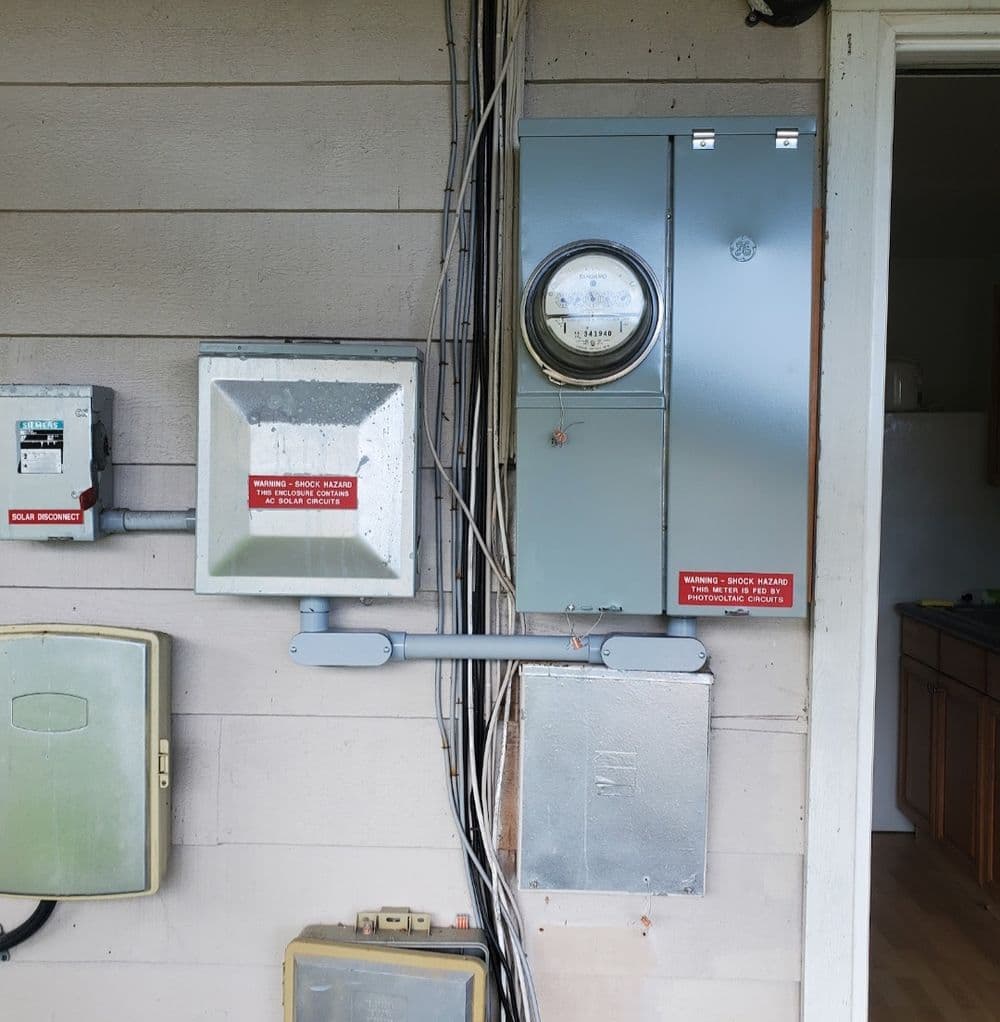 Electrical meter and panels mounted on a house exterior, with warning labels visible.