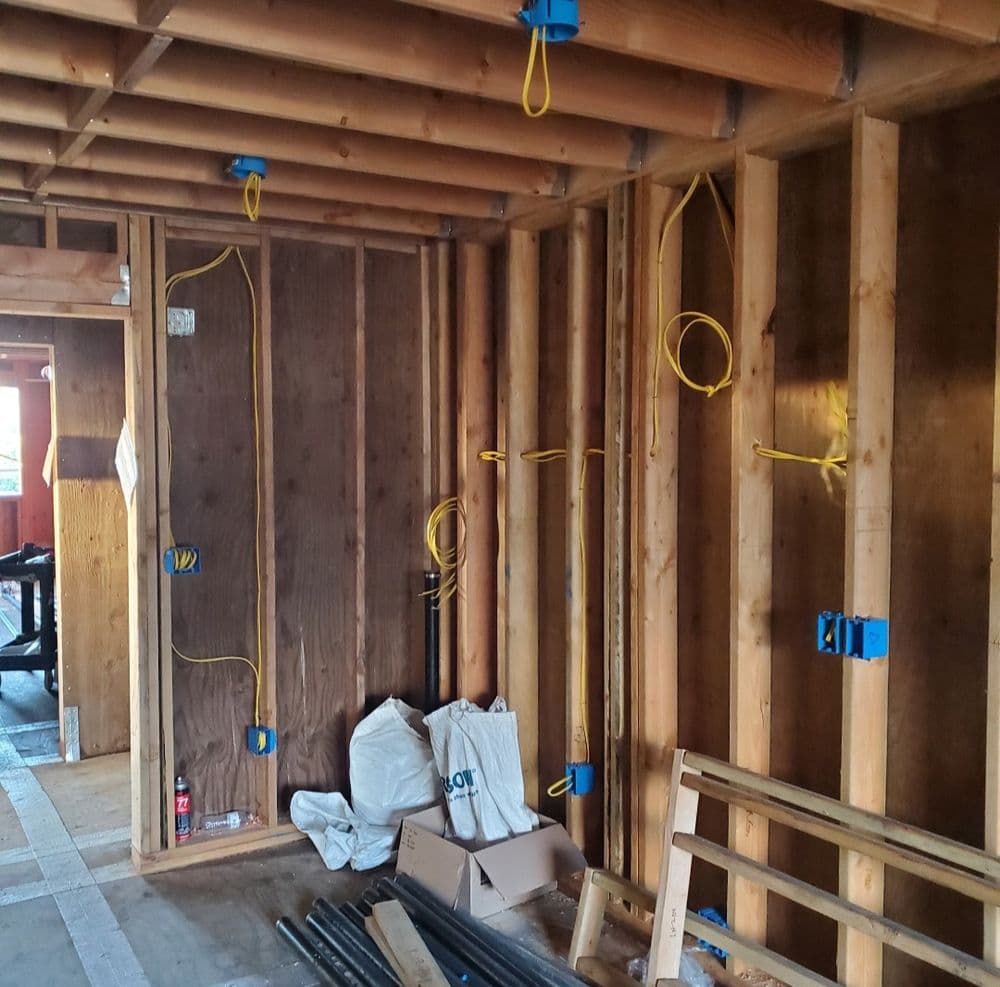 Interior of a construction site showing wooden framing, wiring, and insulation materials.