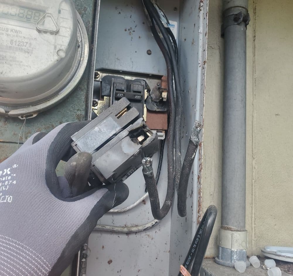 Hand removing a circuit breaker from an electrical panel. Safety gloves visible.
