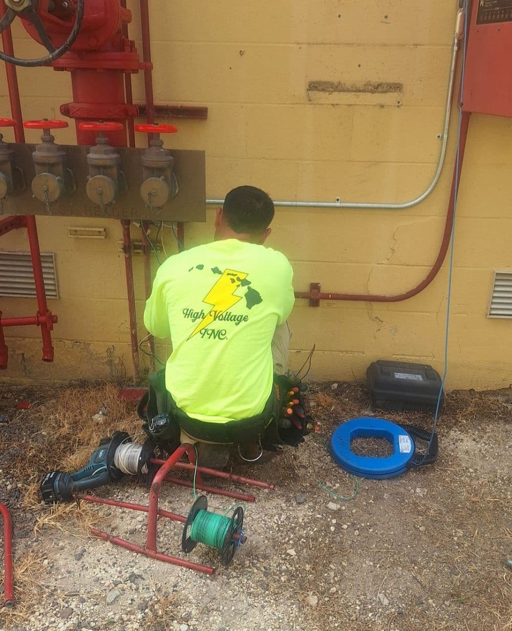 Electrician in high visibility shirt working on electrical equipment near wall.
