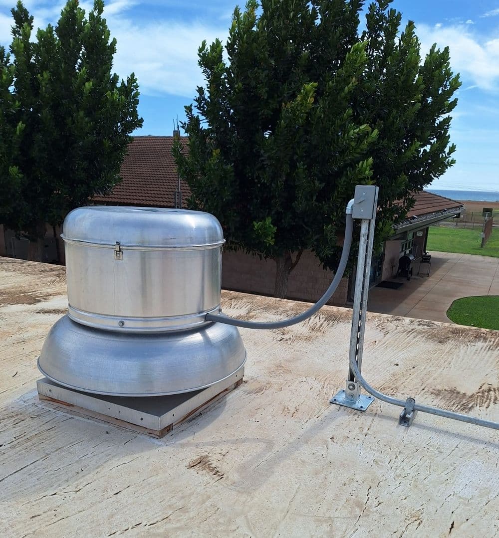 Roof turbine vent with metal casing, mounted on a flat rooftop, against a clear sky.