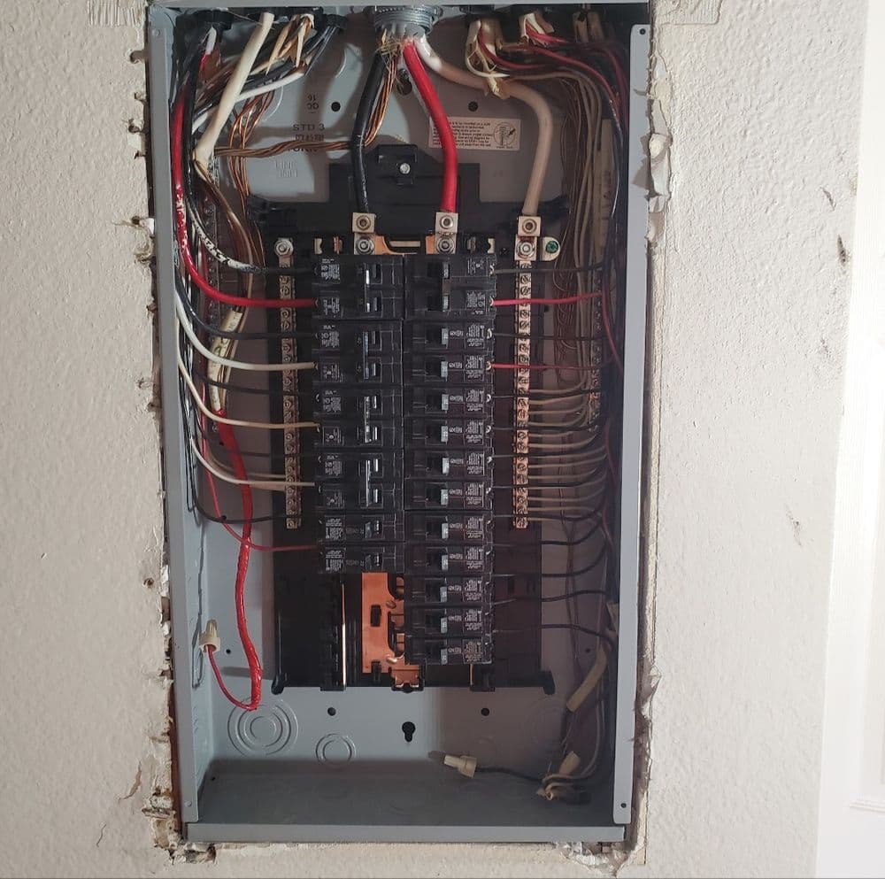 Electrical panel with multiple circuit breakers and visible wiring connections.