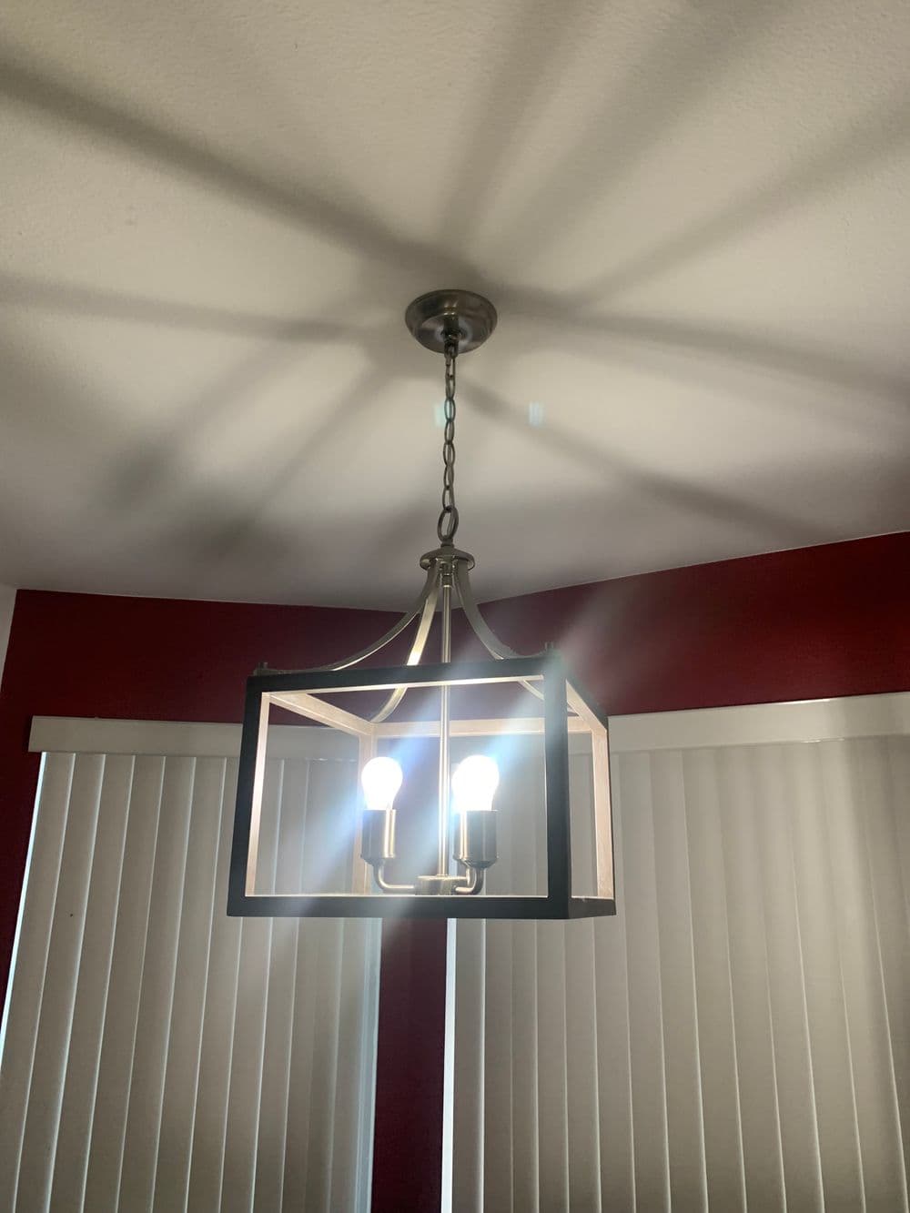 Modern pendant light fixture with geometric design and bright bulbs, casting shadows on the ceiling.