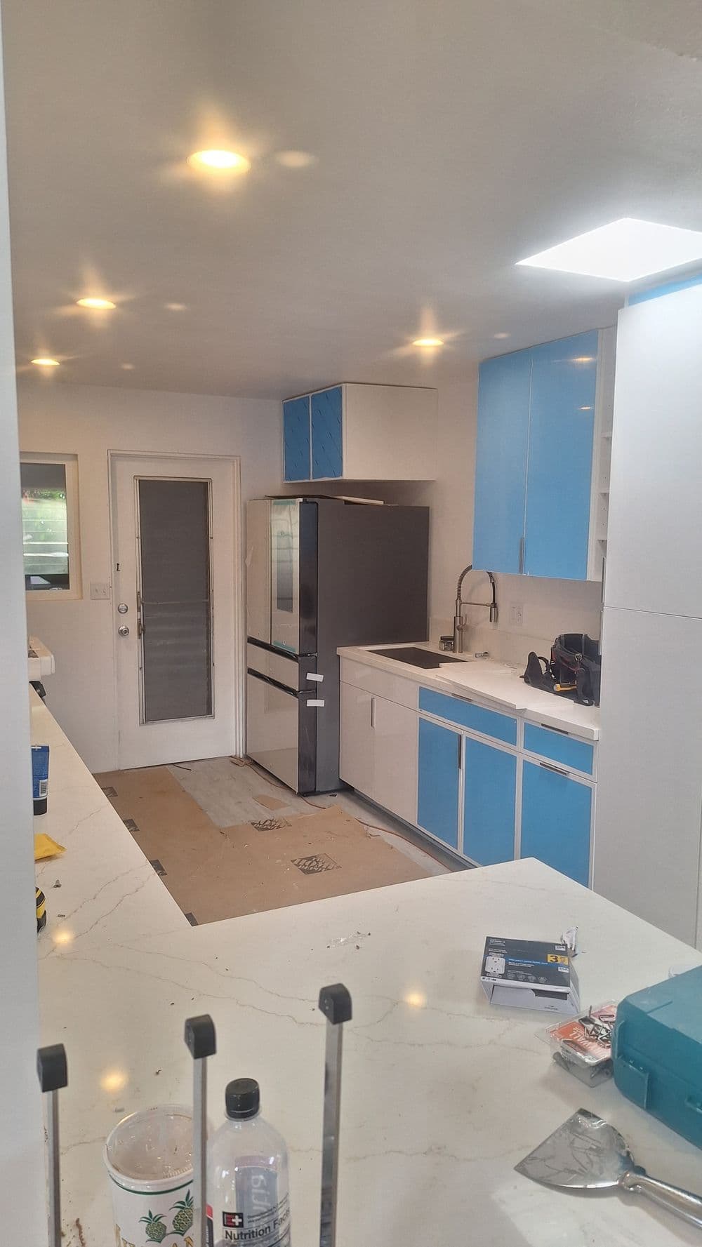 Modern kitchen renovation featuring blue cabinets, stainless steel fridge, and marble countertop.