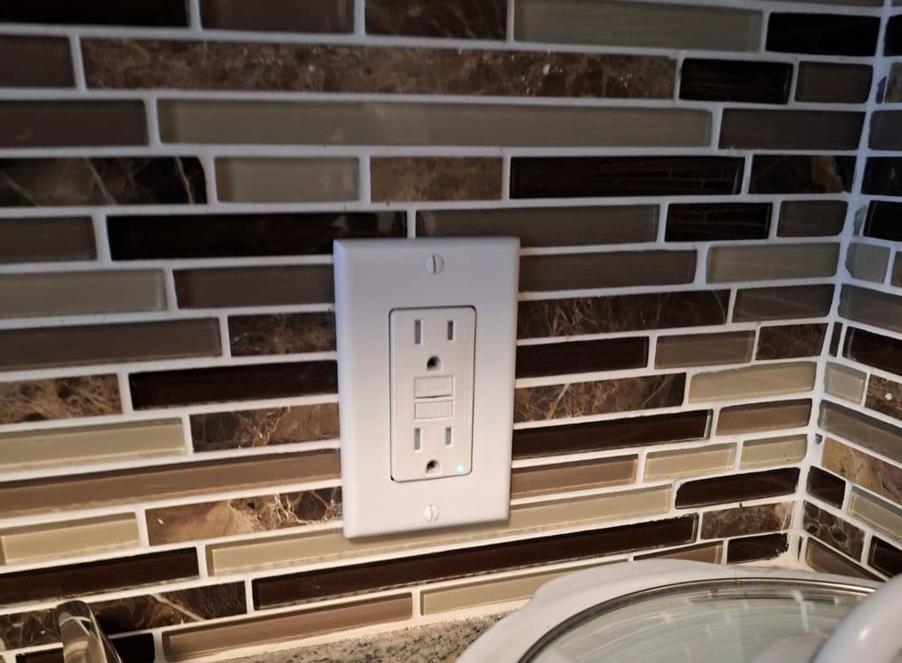 Electrical outlet on a mosaic tile backsplash in a modern kitchen setting.