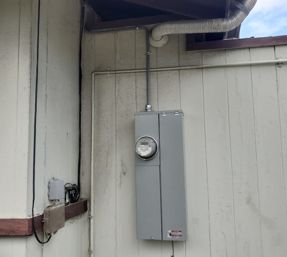 Electric meter mounted on a wall with visible pipes and electrical connections.