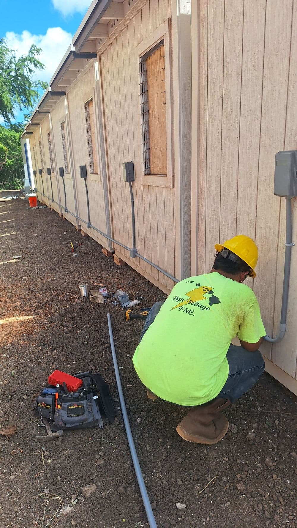 Electrician installing electrical conduits on a new building exterior in work attire.