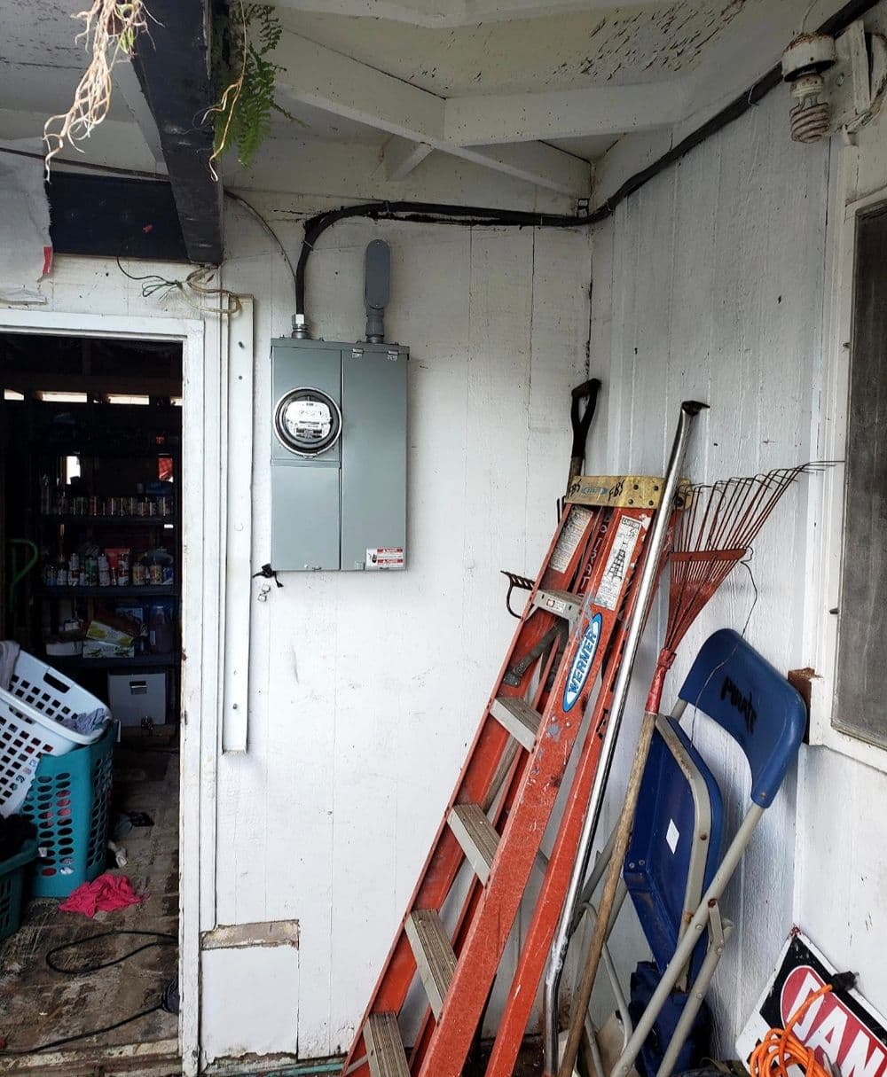 Ladder next to a utility box and cluttered room interior with laundry basket and tools.