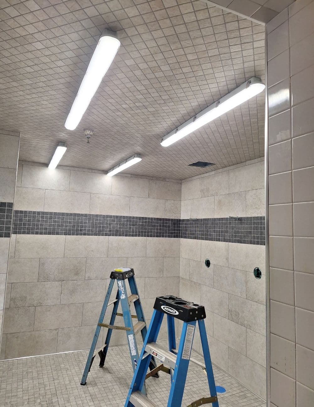 Renovated shower space with modern lighting and a ladder for installation.