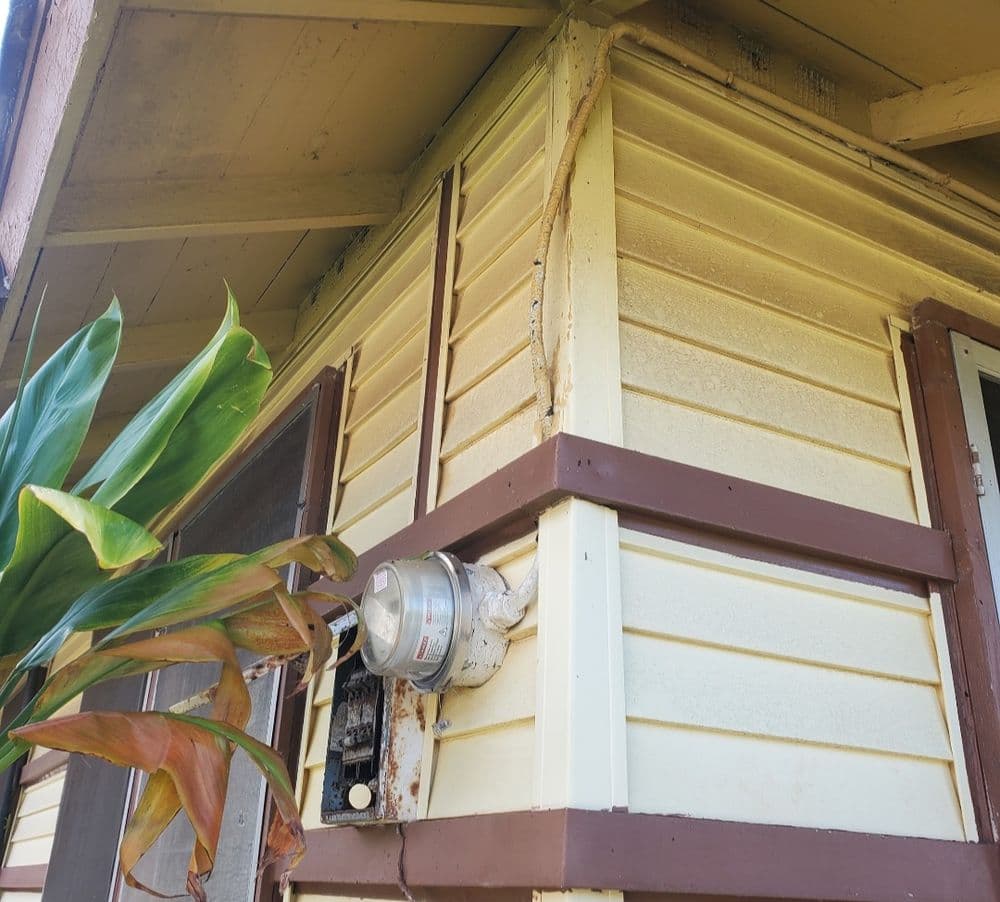 Yellow house exterior showing weathered siding and a visible electric meter.