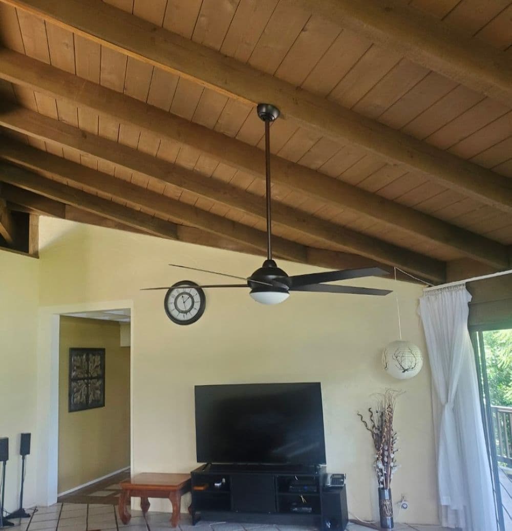 Modern living room with a ceiling fan, TV, clock, and artistic wall decor.