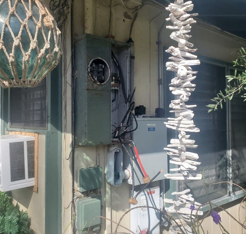 Electrical panel mounted on a wall with decorative driftwood, air conditioning unit nearby.