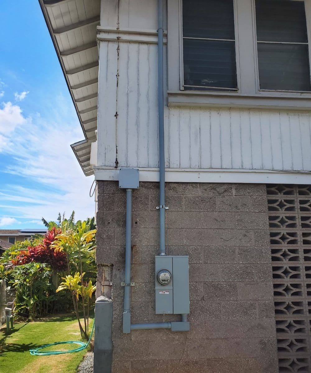 Electrical meter box mounted on a home exterior with pipes running along the wall.
