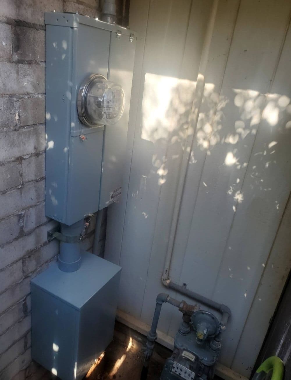 Electric meter and gas meter installation against a brick wall in a utility area.