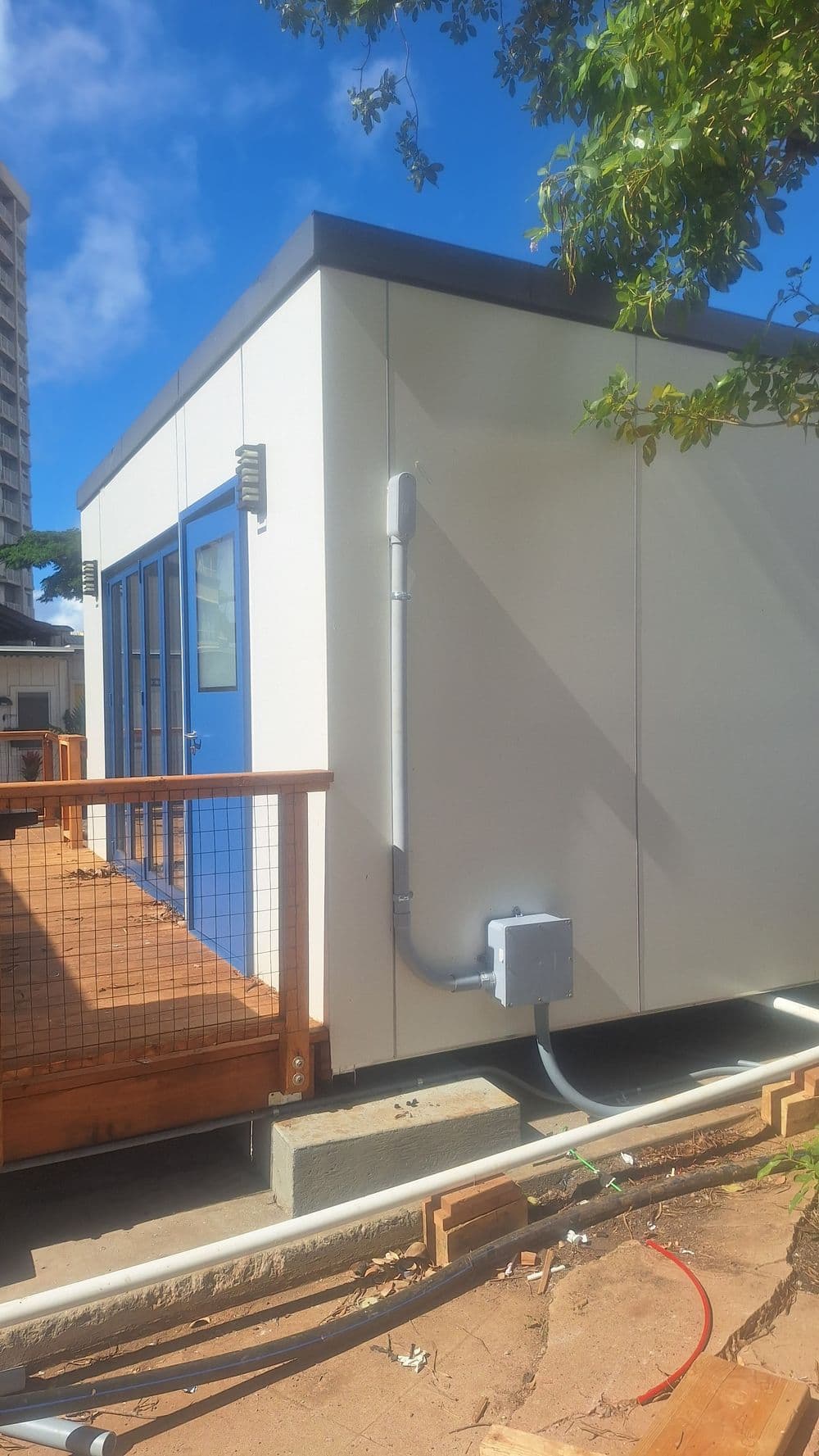 Modern prefabricated building with blue doors, situated on a wooden deck.