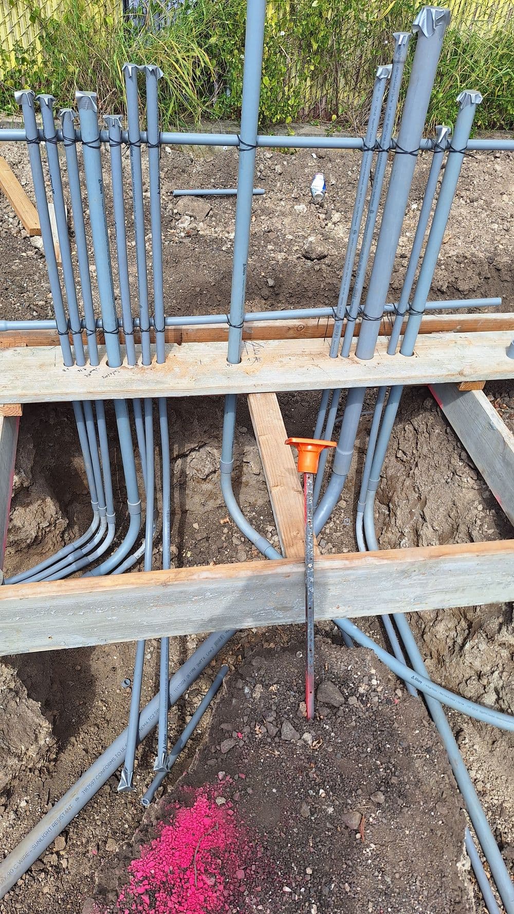 PVC pipes and conduit arranged in a construction site trench with wooden planks.