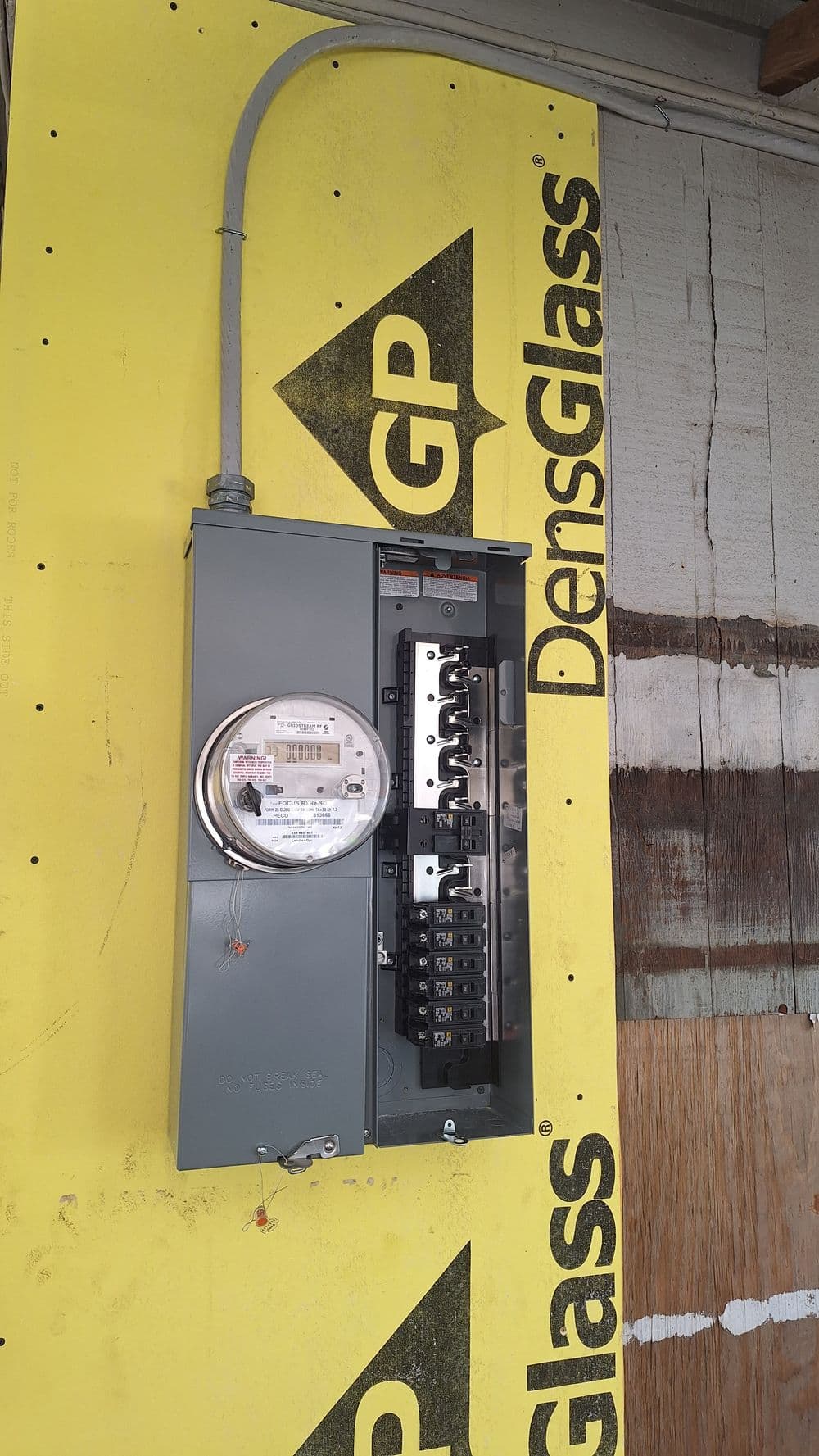 Electrical meter and circuit breaker panel mounted on yellow DensGlass sheathing.