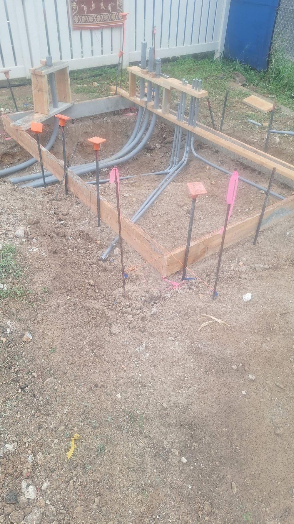 Construction site showing a detailed foundation frame with electrical conduits and markers.